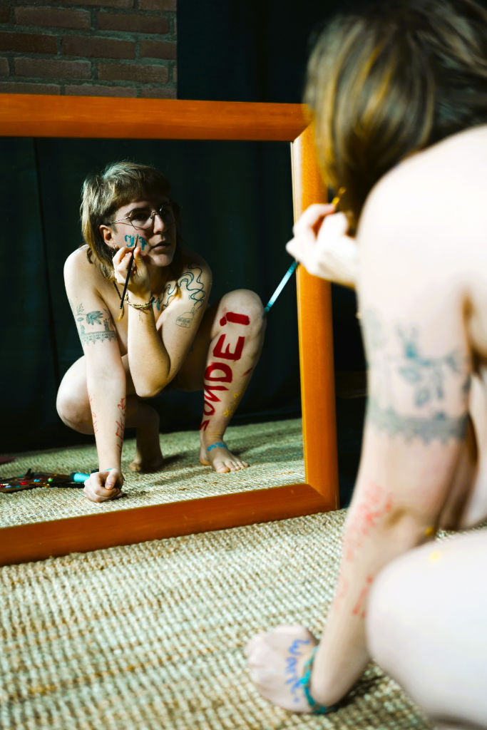 Naaktmodel Rosa kijkt in de spiegel terwijl ze op haar gezicht schildert