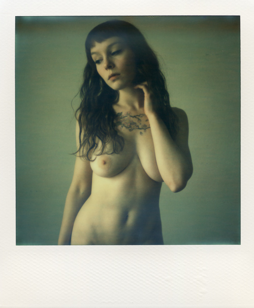 Polaroidfoto van een vrouw met een tatoeage op haar borst en lang haar tot op haar borsten