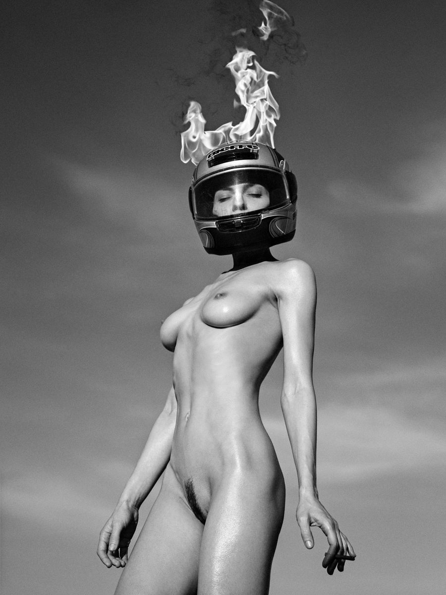 Naakte vrouw in zwart-wit, kikvorsperspectief, met een brandende motorhelm op haar hoofd