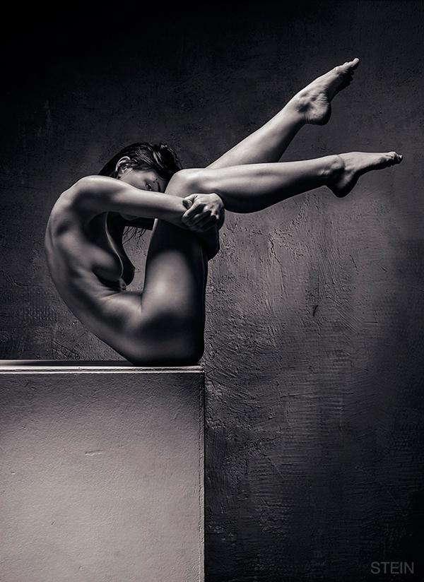 Danseres poseert naakt met haar benen hoog in de lucht op een blok in de studio